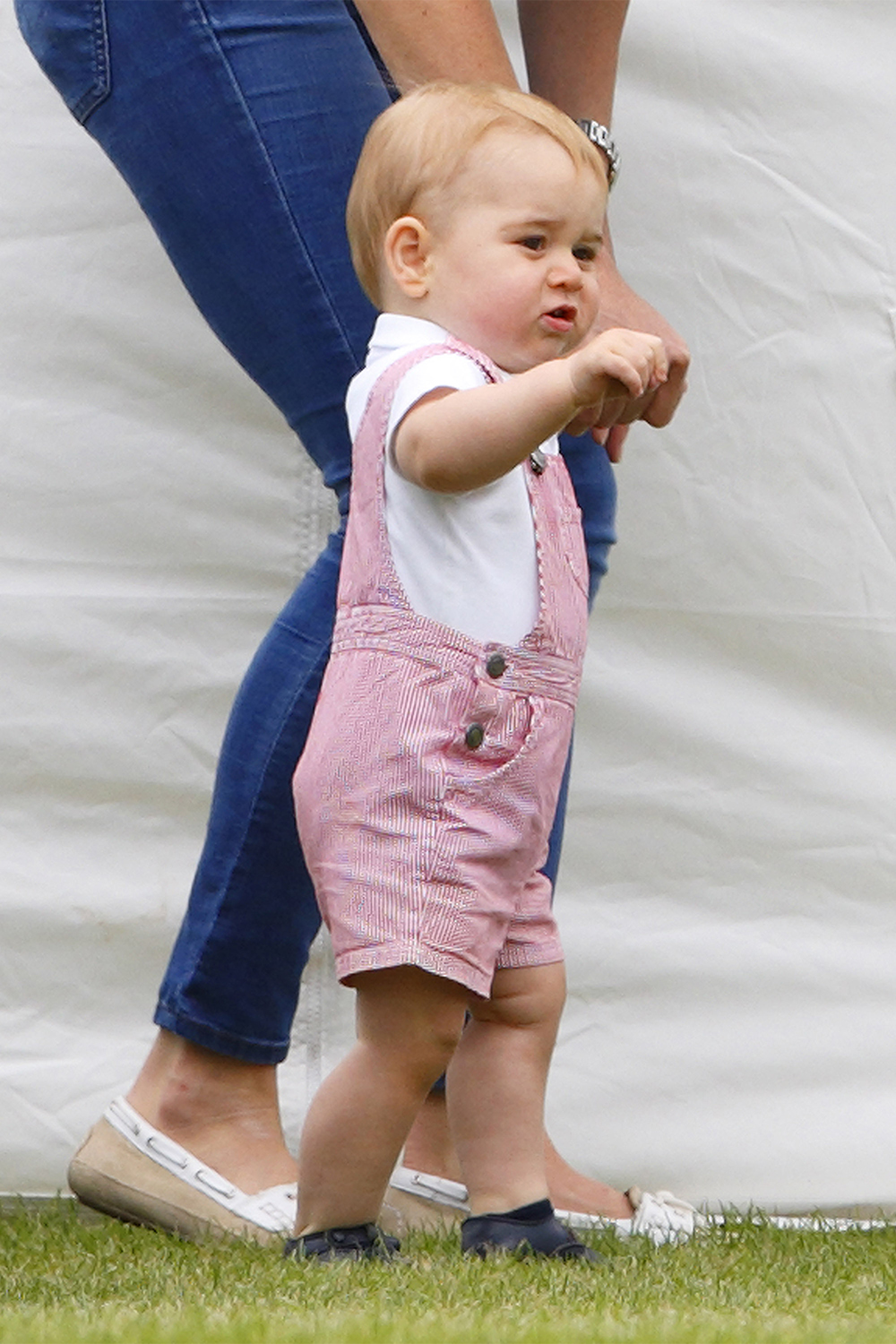In a pair of red and white stripe dungarees watching his father Prince William and Uncle Harry play in the Jerudong Trophy charity polo match at Cirencester Park Polo Club on June 15, 2014.