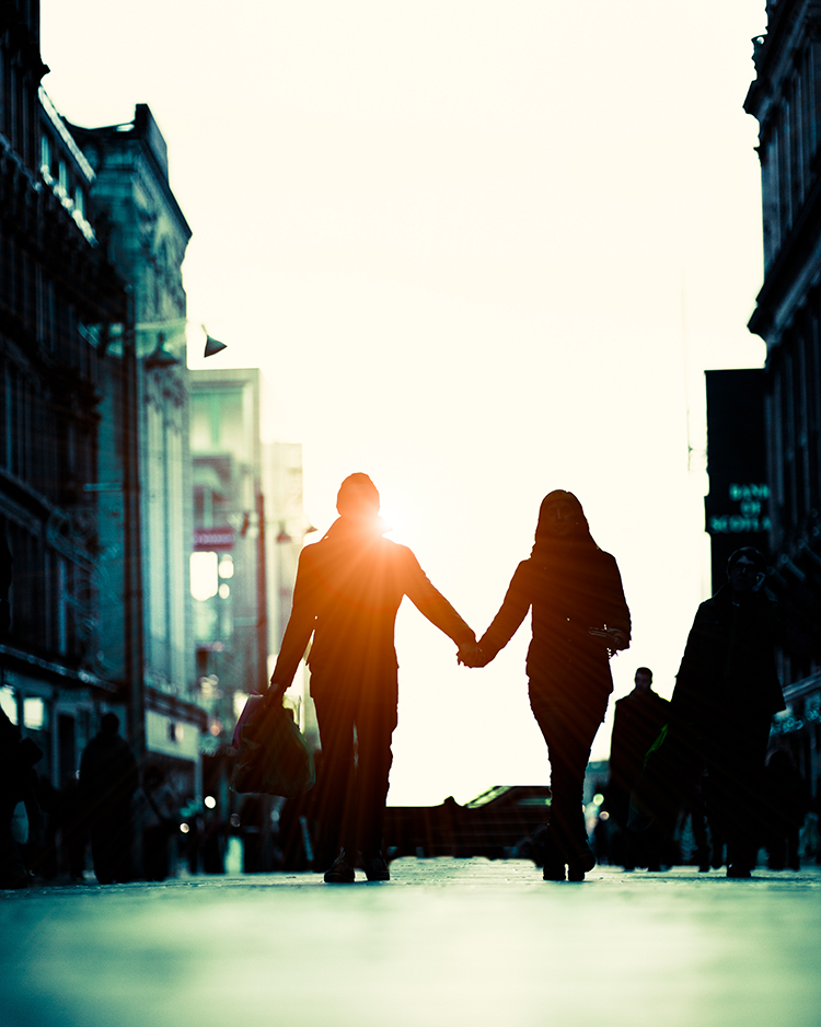 Young couple walking hand in hand down city street with sun flare.