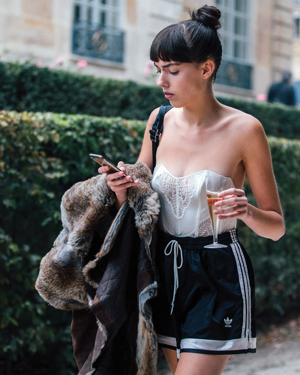 Model Kye Howell checks her phone and drinks champagne, while wearing a white corset top, black sporty Adidas shorts and the attitude of our dreams after the Dior show in September 2016.