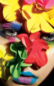 A model with colourful smears of makeup surrounded by fake flowers poses for MAC cosmetics' makeup campaign - C Shock 
