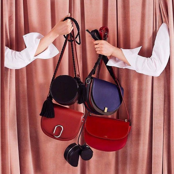 Two hands clutch a collection of designer handbags