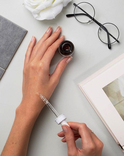 Hands trial a bottle of The Ordinary skincare on a flatlay table