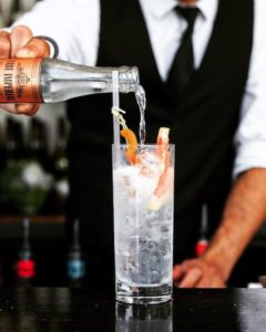 A waiter's hands pours a gin and tonic at a bar