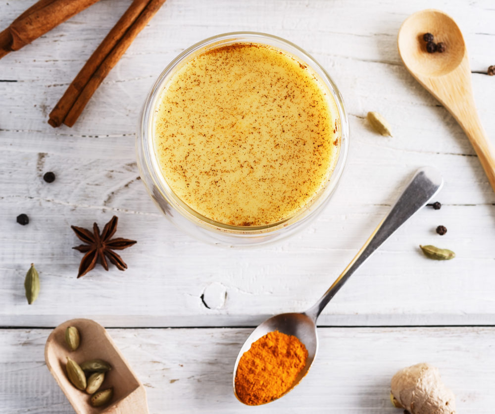 Top view image of turmeric latte, spices and bottle of milk over white wooden table