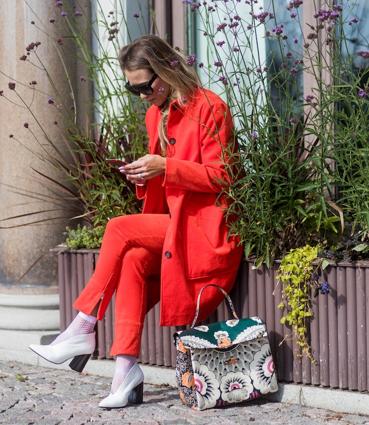 Line Langmo writting a text with her phone wearing red Ganni jacket and pants, white tshirt with rainbow print outside Stylein