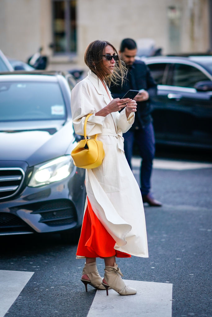PARIS, FRANCE - JANUARY 22: A guest wears sunglasses, a white trench coat, an orange dress, a yellow bag, holds a smartphone, outside Proenza Schouler, during Paris Fashion Week -Haute Couture Spring/Summer 2018, on January 22, 2018 in Paris, France. (Photo by Edward Berthelot/Getty Images)