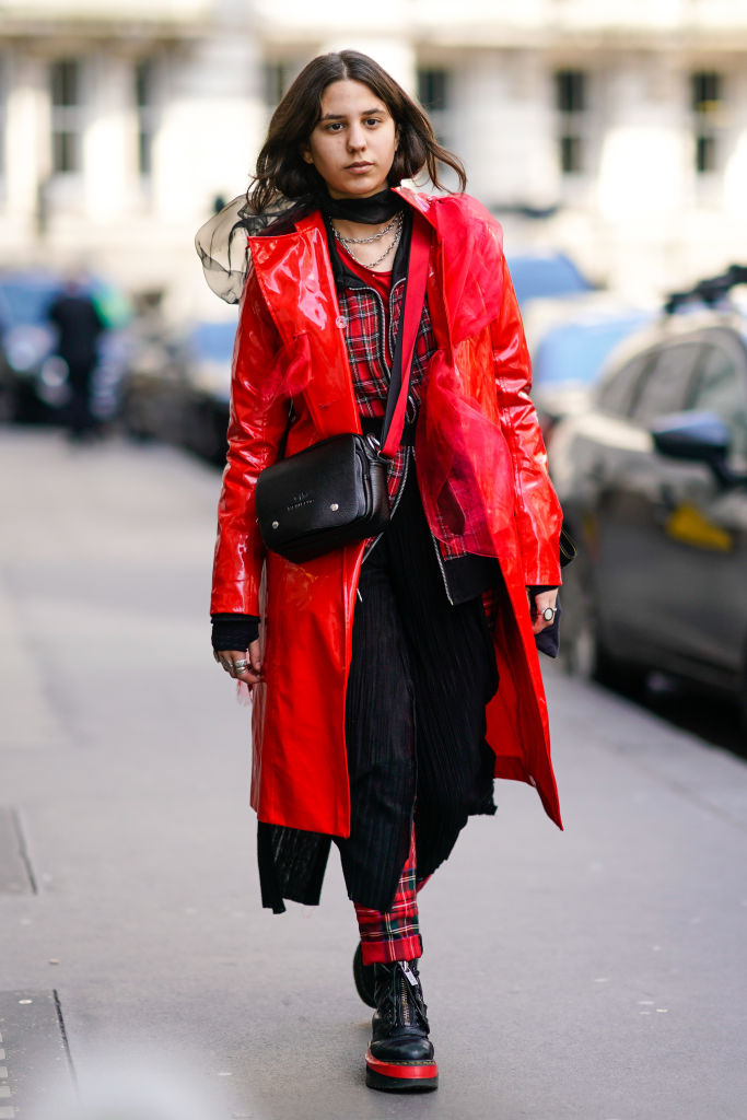 LONDON, ENGLAND - FEBRUARY 17: A guest wears a red plastic coat, checked pants, a black bag, during London Fashion Week February 2018 on February 17, 2018 in London, England. (Photo by Edward Berthelot/Getty Images)