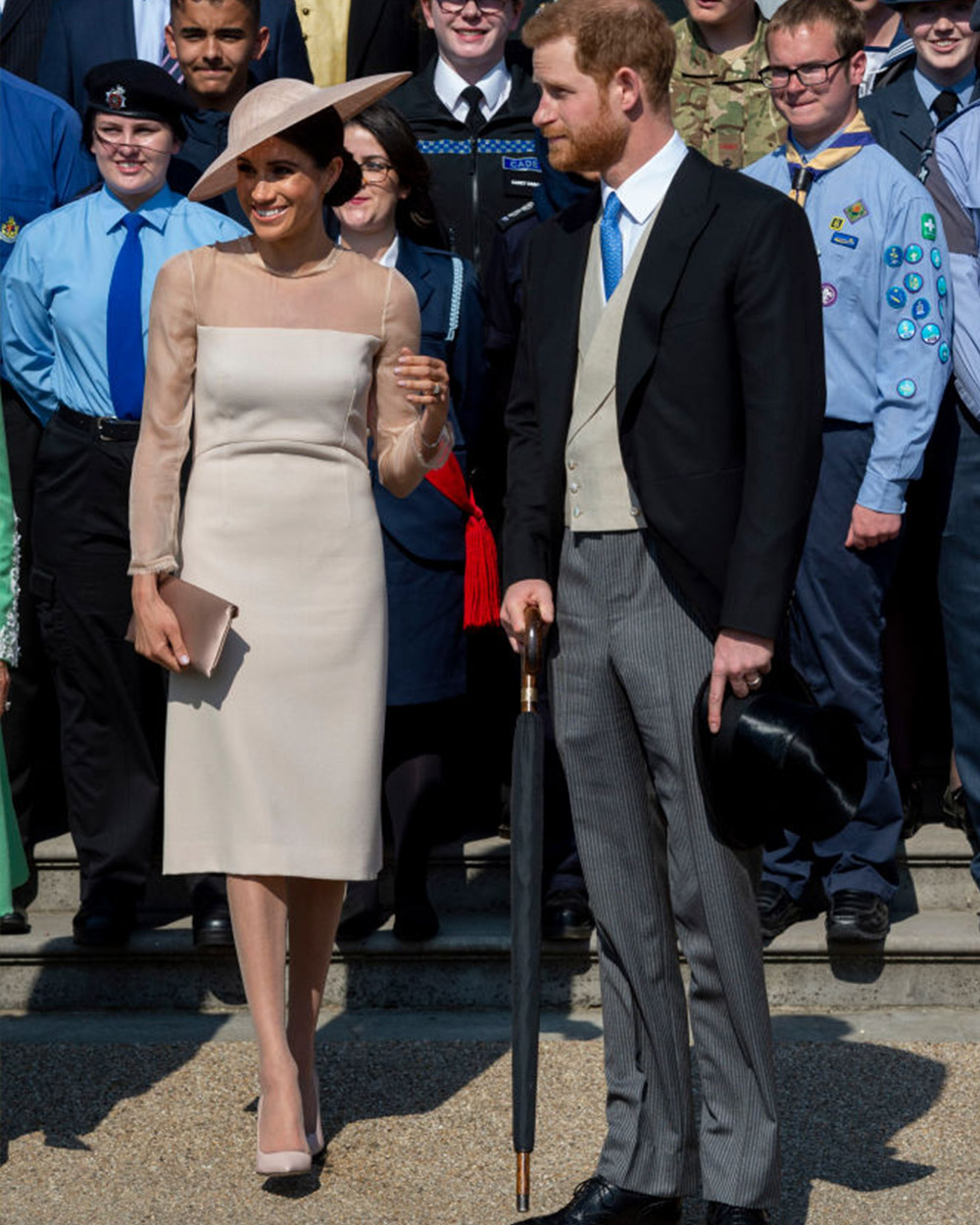 May 22, 2018: Stepping out as the Duchess of Sussex, Meghan sports her post-wedding glow to Prince Charles' 70th birthday garden party at Buckingham Palace. Meghan wears a blush, sleeved sheath dress by GOAT, a bespoke Phillip Treacy hat, Vanessa Tugendhaft rose-shaped diamond earrings and Wilbur & Gussie oyster silk clutch.