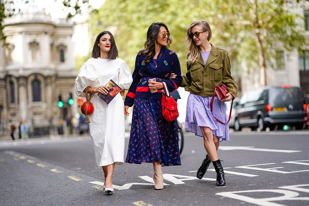 A guest (L) wears a white dress, a guest (M) wears a blue skirt, a guest (R) wears a green jacket, during London Fashion Week September 2018 on September 14, 2018 in London, England. (Photo by Edward Berthelot/Getty Images)