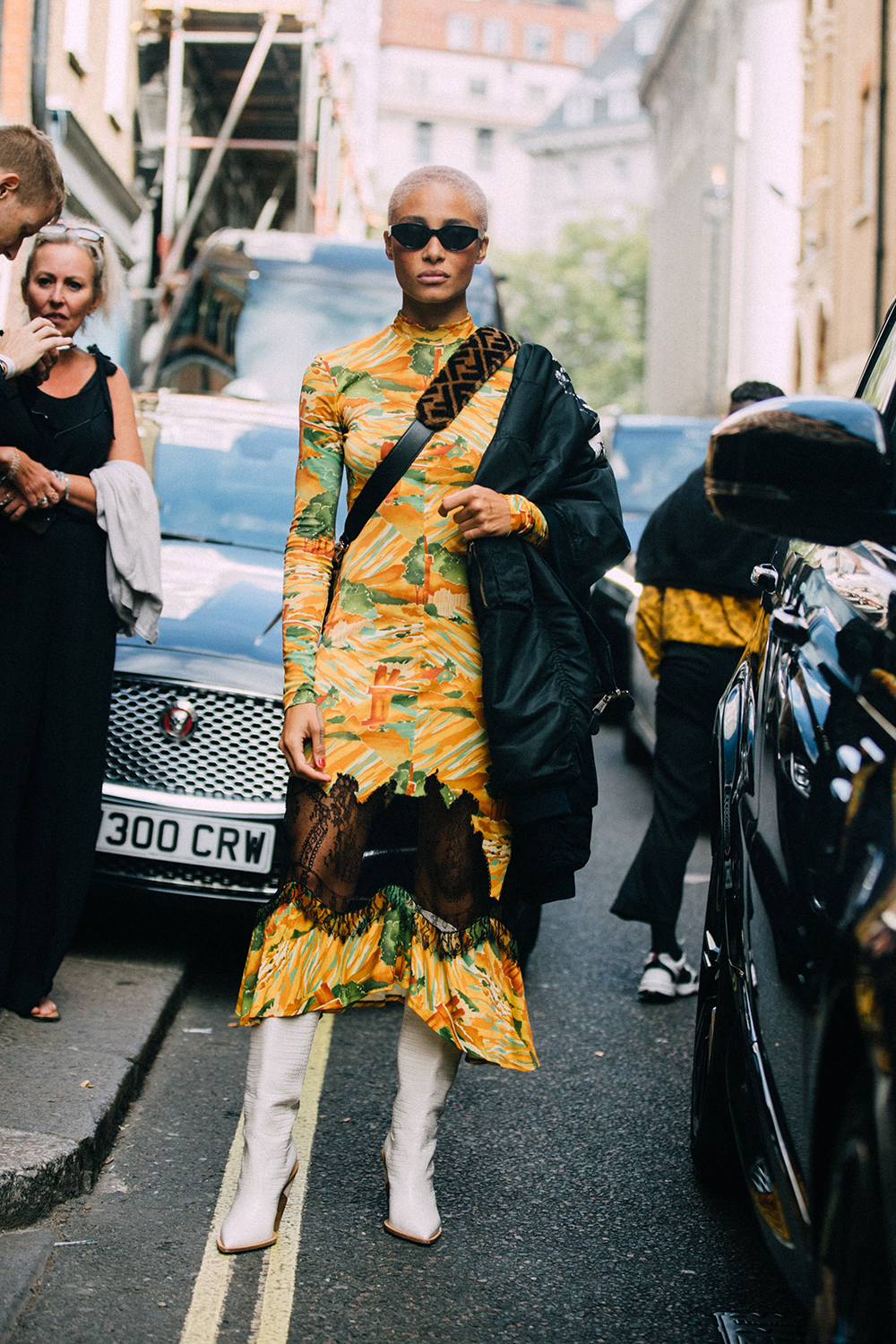 LONDON, ENGLAND - SEPTEMBER 15: Model Adwoa Aboah wears black sunglasses, a Fendi fur cross-body bag, yellow print dress, white boots, and a bomber jacket on one shoulders after the Molly Goddard show during London Fashion Week September 2018 on September 13, 2018 in London, England.