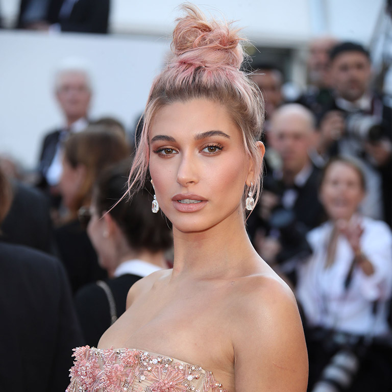 May 2018: Hailey sweeps her tousled rosey strands into a messy top knot with intentional brushed out tendrils around her face to soften the look.  Perfect for: Giving an otherwise formal look a modern sensibility. However, take the earrings away and you're looking at casual Friday vibe. You've been warned. 