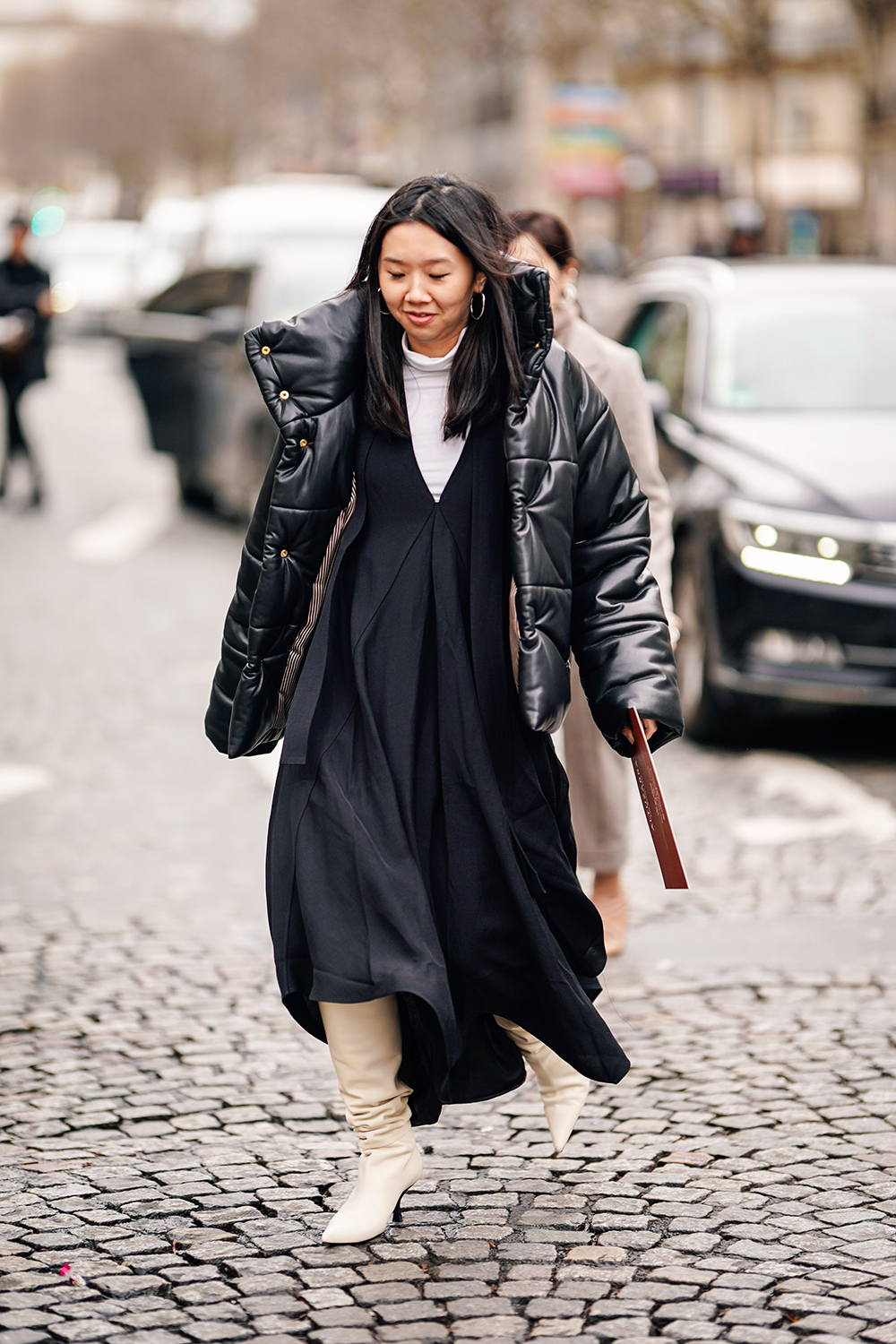 PARIS, FRANCE - MARCH 02: A guest wears earrings, a black puffer jacket, a white turtleneck, a black low-cut pleated dress, white pointy high-heeled boots, outside Altuzarra, during Paris Fashion Week Womenswear Fall/Winter 2019/2020, on March 02, 2019 in Paris, France. (Photo by Edward Berthelot/Getty Images)