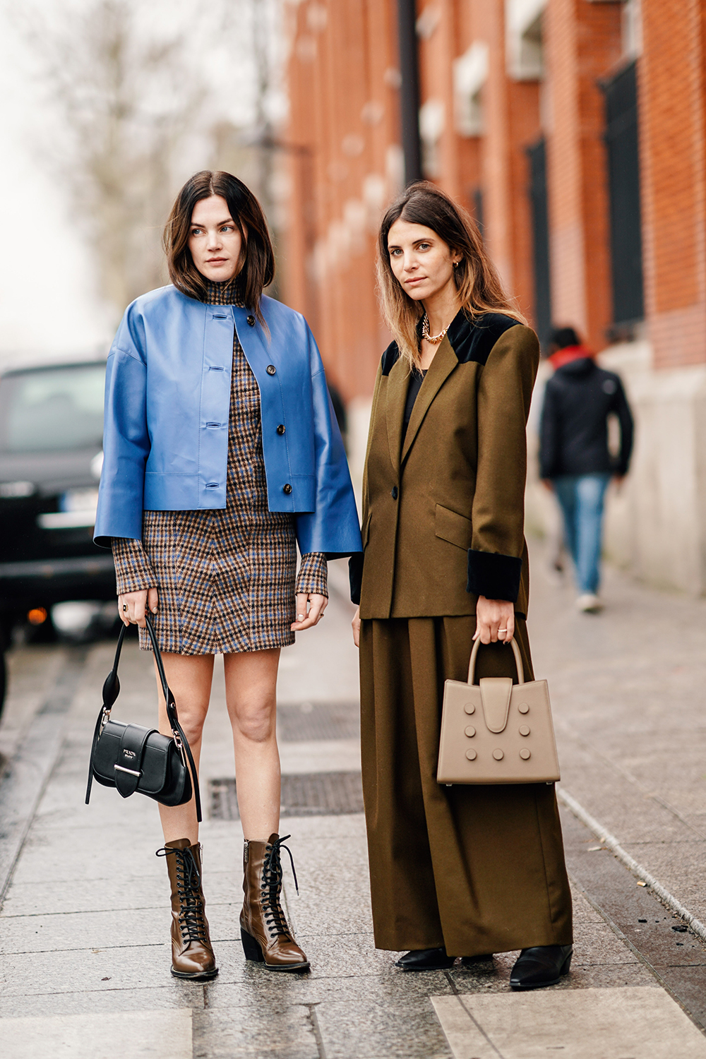 PARIS, FRANCE - MARCH 01: Madelynn Furlong (L) wears a turtleneck brown and blue tweed dress, a lavender-blue leather jacket, a black Prada bag, brown pointy lace-up boots ; Erika Boldrin (R) wears a golden necklace, a brown pantsuit with black velvet cuffs, black velvet insert at the shoulder, wide-leg pants, a beige bag,outside Nina Ricci, during Paris Fashion Week Womenswear Fall/Winter 2019/2020, on March 01, 2019 in Paris, France. (Photo by Edward Berthelot/Getty Images)