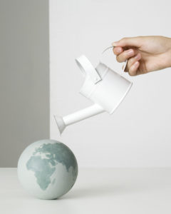 Hand holding watering can over small globe
