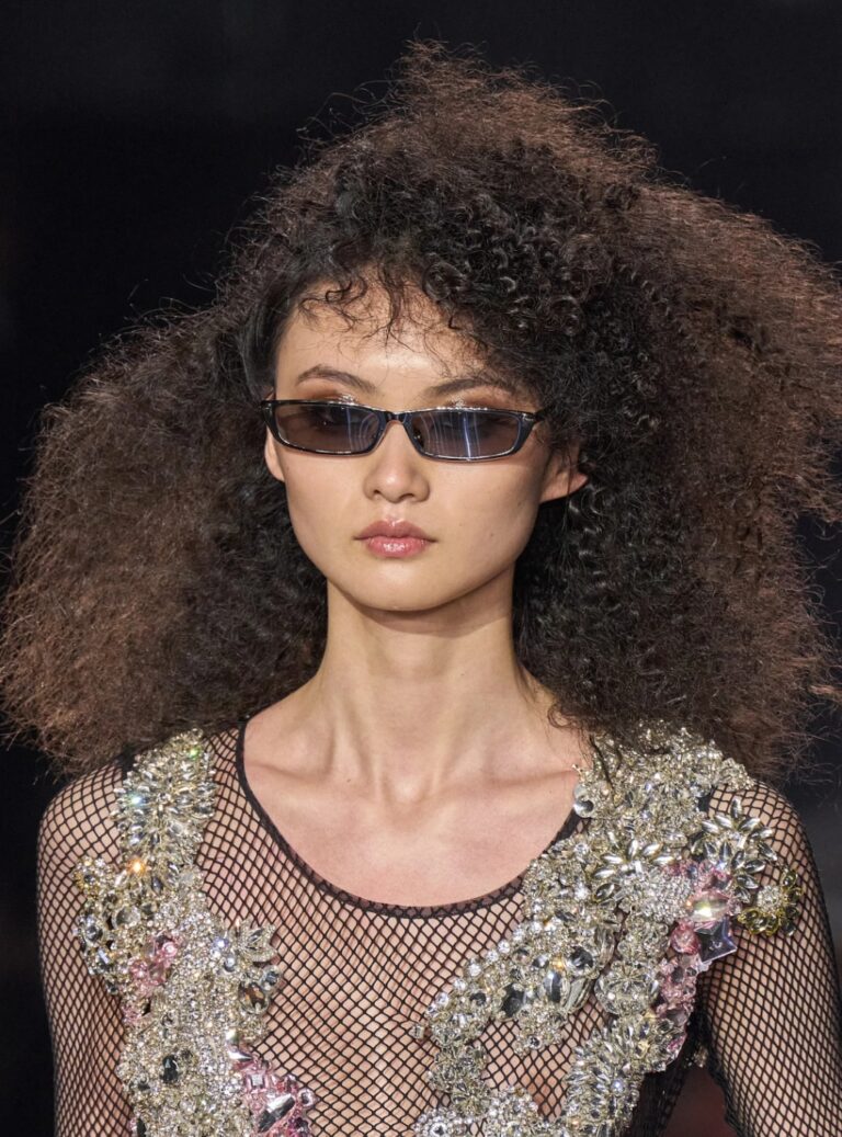 Detail shot of model from Tom Ford runway spring 2023 ready-to-wear collection. Woman has high-volume brushed out micro-curls.