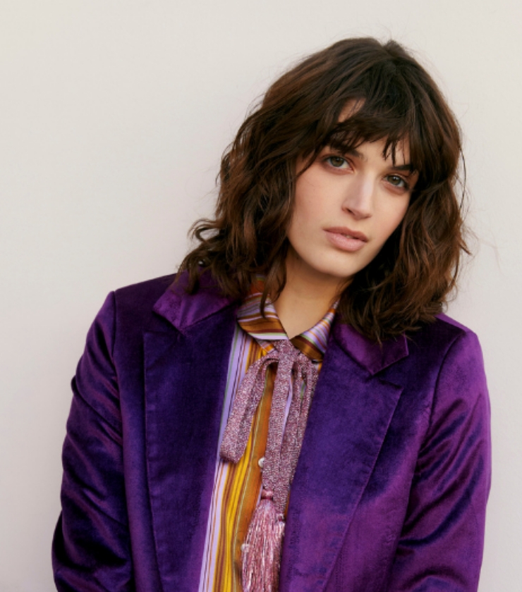 Image of a model woman wearing a purple velvet blazer and brunette 'shullet' hairstyle also known as the shaggy mullet.