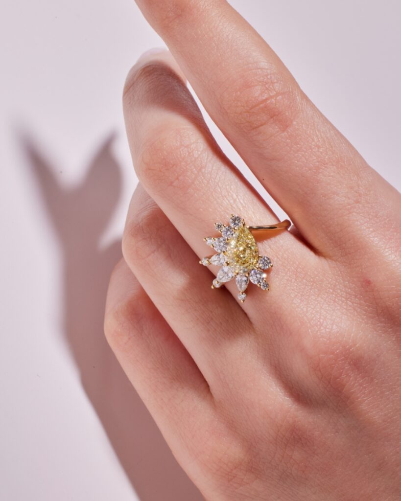 Featuring a GIA certified Fancy Light Yellow pear cut diamond placed diagonally on the band, accented by a medley of round and pear cut white diamonds in an open halo; set in 18ct yellow gold.