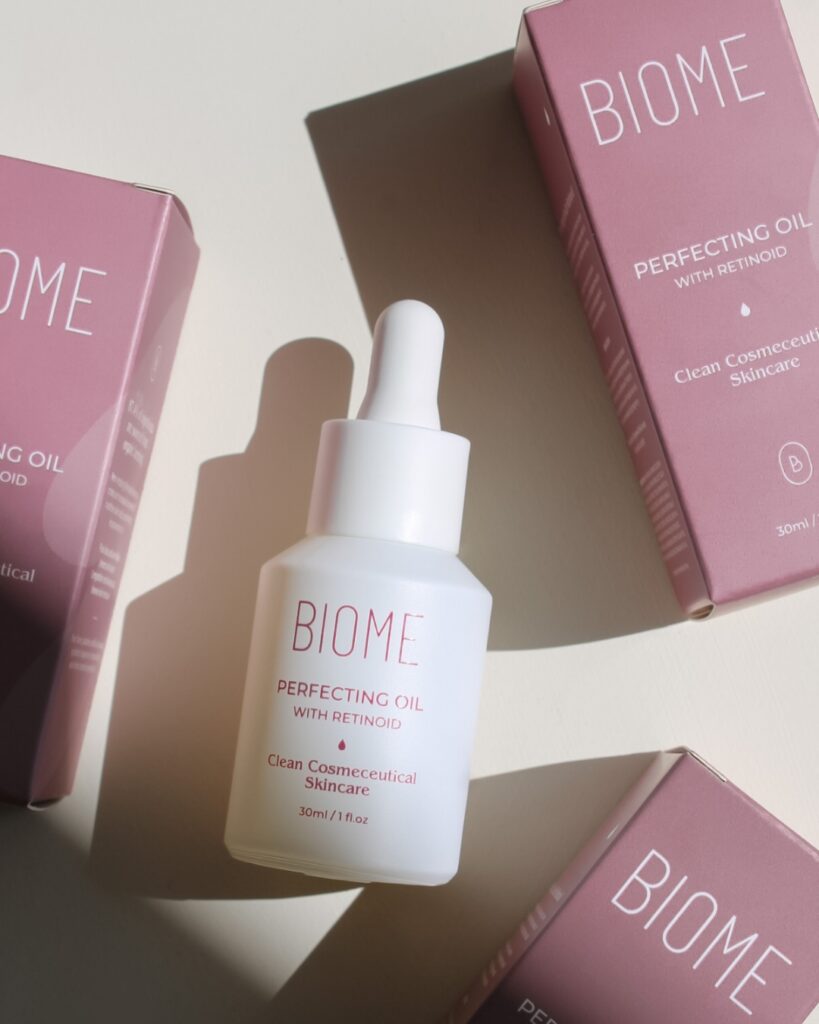 ebecca Spencer, founder of Biome Skin and Beauty, smiling in her skincare clinic, showcasing her Biome Perfecting Oil.